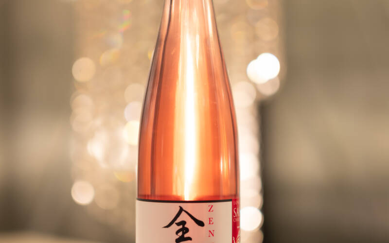 Image of a bottle of Plum Sake from Zenkuro Brewery in Queenstown NZ. Postitioned in front of a chandelier at the 2025 Sakura and Sake Dinner at The GEorge hotel